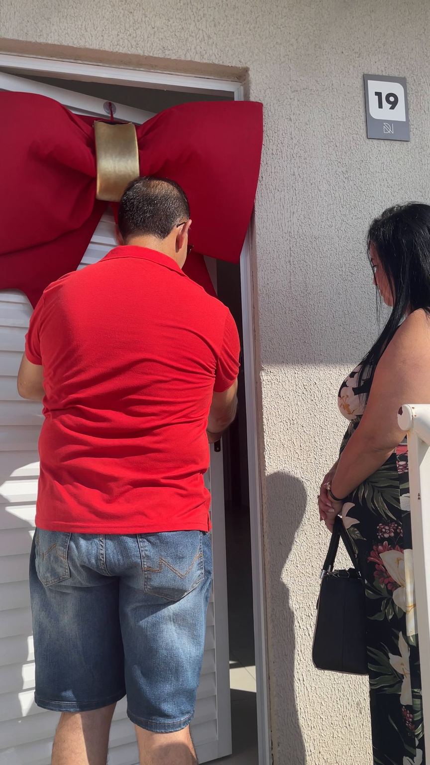 Morador abre a porta com laço vermelho.