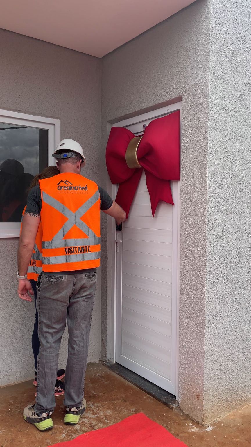 Visitante abre a porta com laço vermelho.