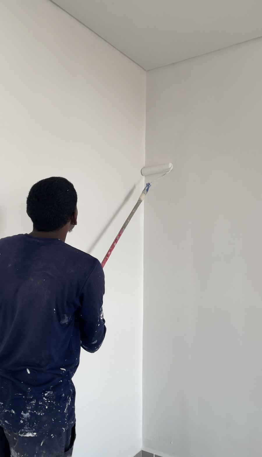 Pintor passa rolo na parede de um cômodo.