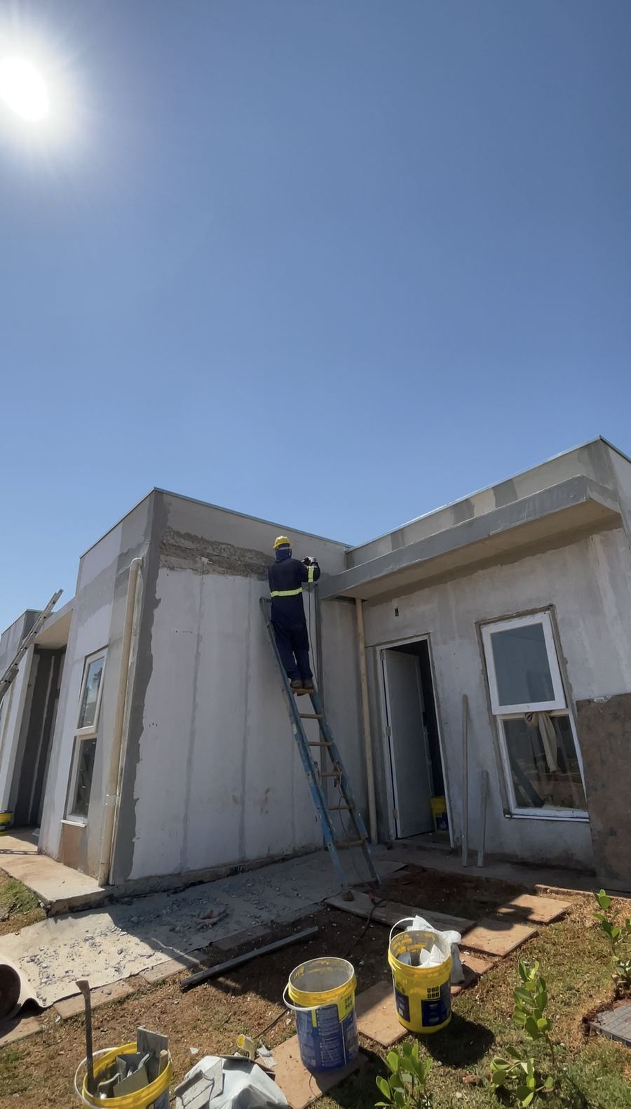 Casa em acabamento, com um profissional na escada e latas de tinta na frente.