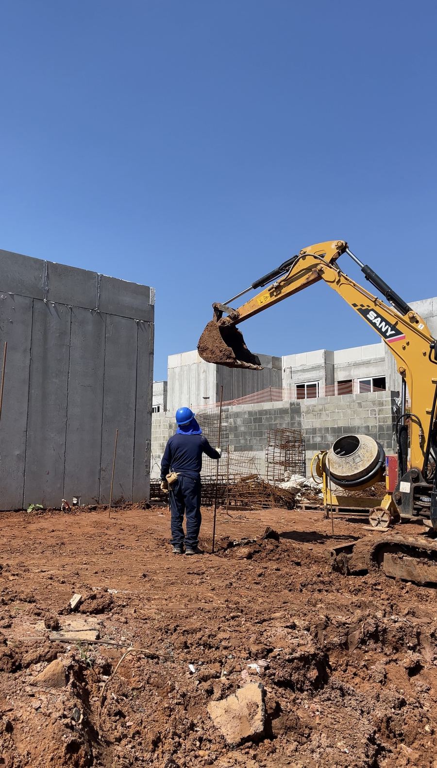Escavadeira prepara o terreno ao lado das paredes de concreto.