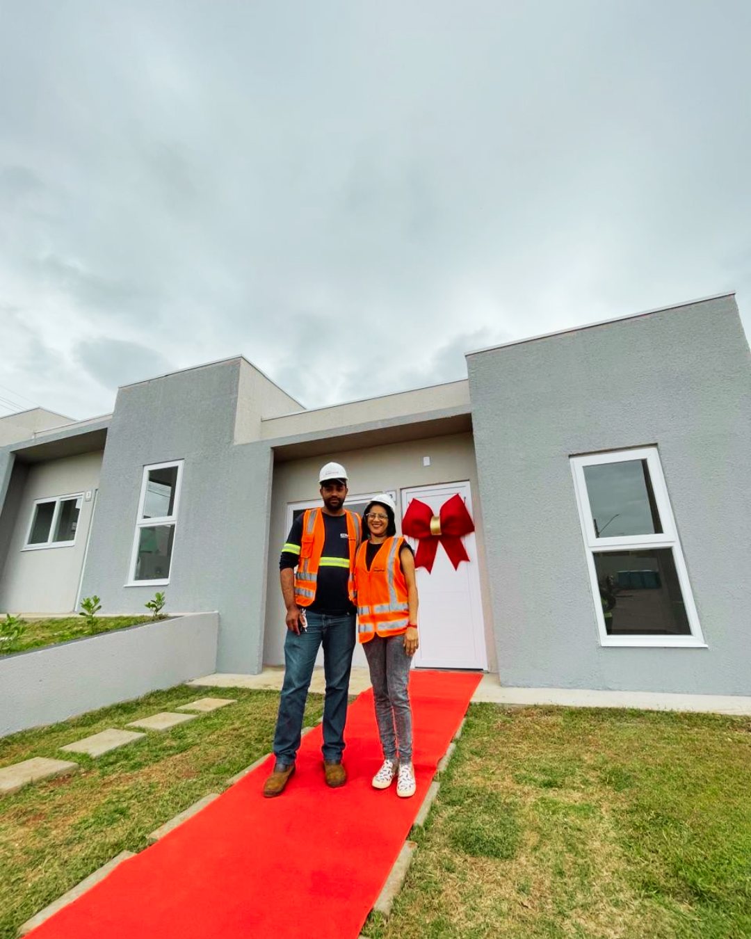 Equipe da Área Incrível no tapete vermelho em frente à casa entregue, com o laço vermelho na porta.